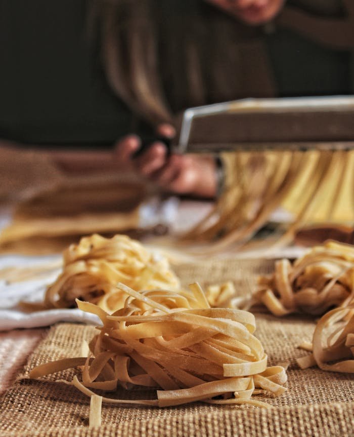 Close-up of handcrafted pasta being made with a pasta machine, showcasing the artisanal process indoors.