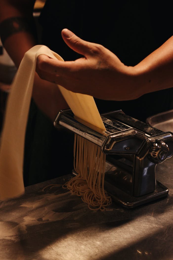 Close-up of hands preparing fresh pasta using a traditional pasta machine.