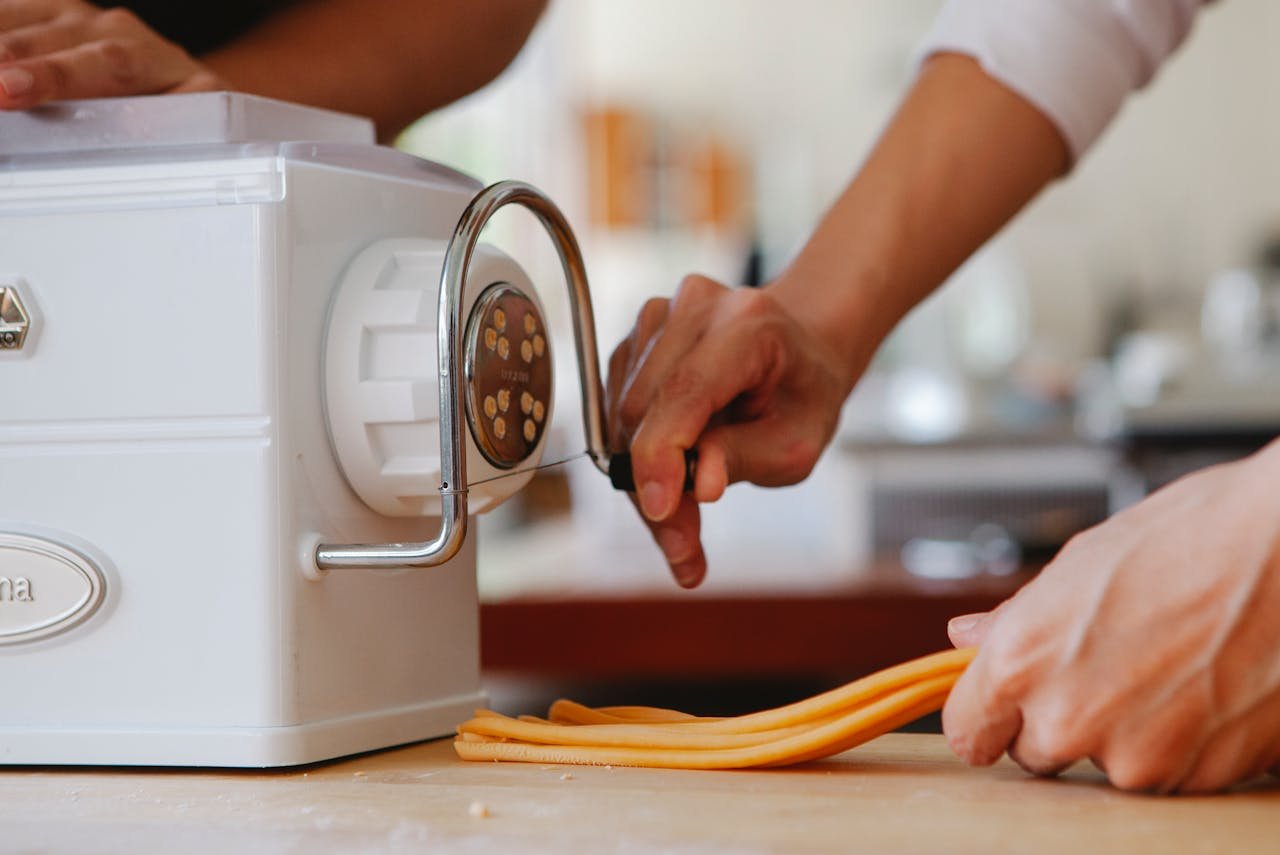 about-us Close-up of hands using a pasta maker to prepare fresh pasta indoors.