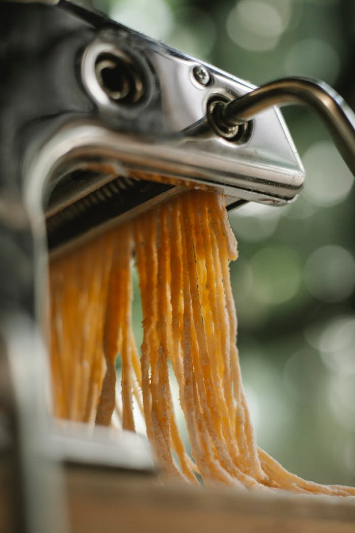 Close-up of fresh pasta being made with a manual pasta machine indoors.