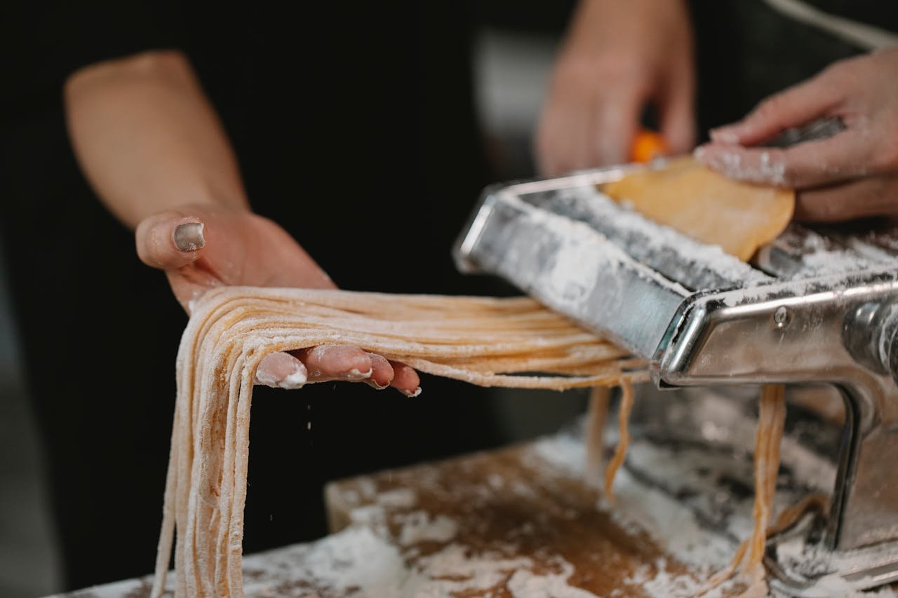 Fresh pasta being prepared with a machine in a kitchen setting.